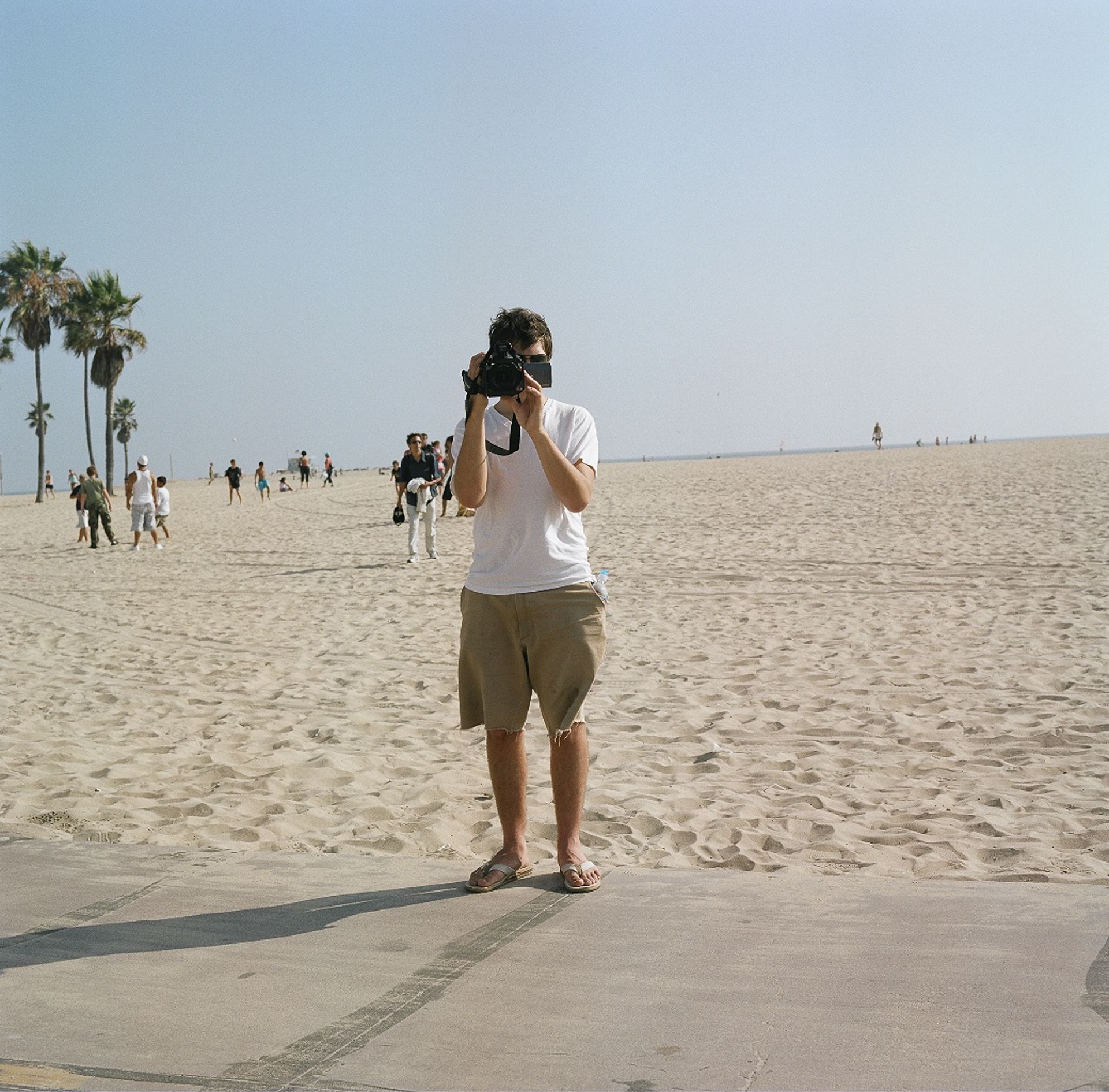 A young Dan photographing on a wide sandy beach lined with palm trees