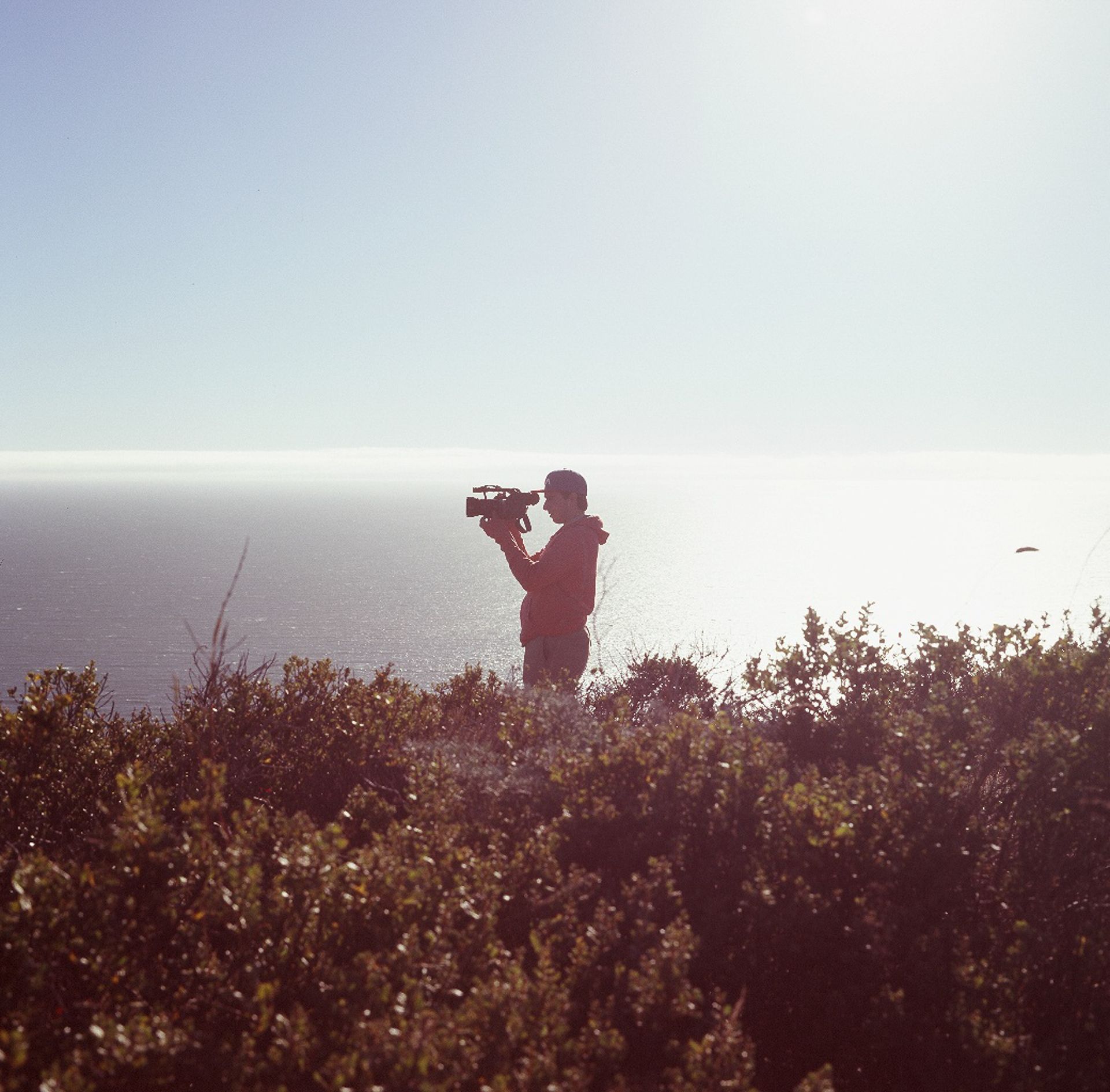 A silhouette filming over a hazy coastline from a clifftop