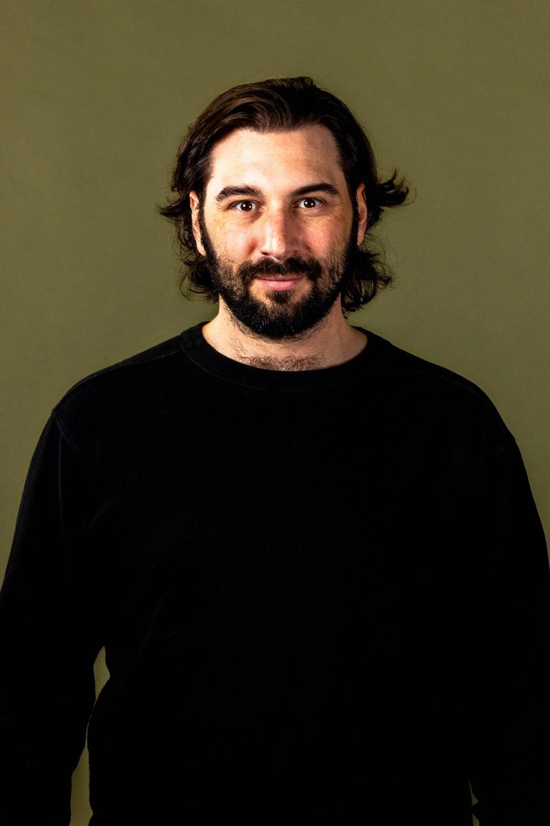 Portrait of Dan Mannes in a black sweater against an olive backdrop