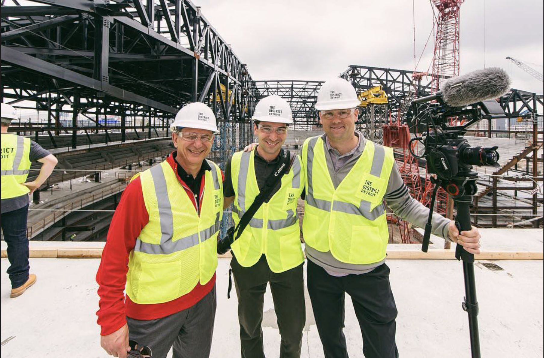 Three people in hard hats and safety vests on the Little Caesars Arena construction site