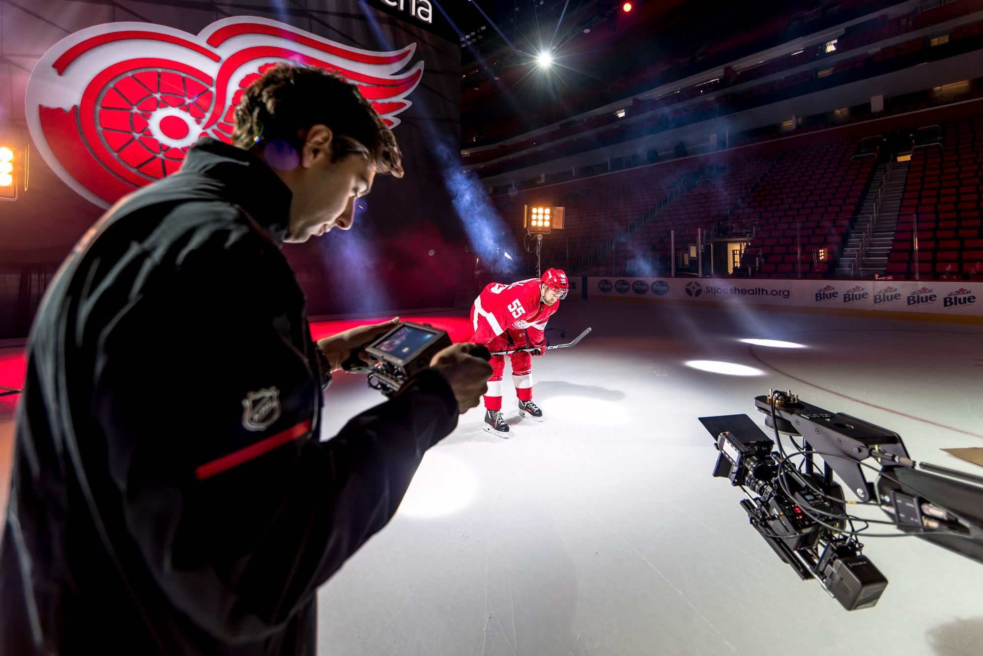 Dan monitoring a camera rig beside the ice as a Red Wings player is lit by spotlight